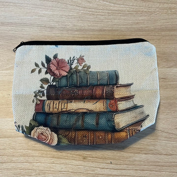 Das Produktbild zeigt ein beiges Täschchen aus Leinen, auf dem ein gemalter Bücherstapel im Vintage Stil und zwei altrosafarbene Blumen, die darauf und davor dekoriert sind, abgebildet ist.